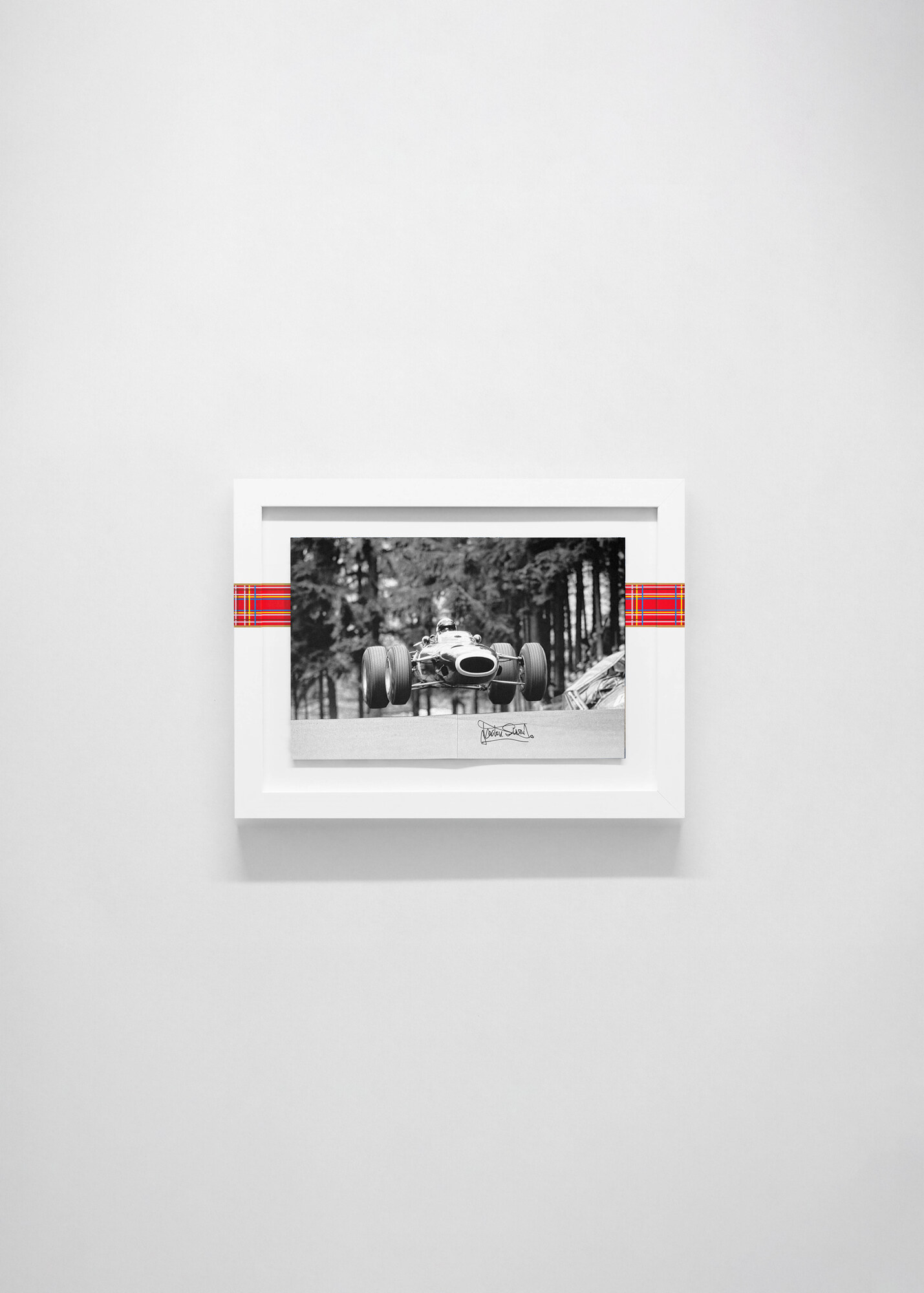 Closed on a white wall, showing a black-and-white spread of a car airborne between trees, signed on the print face.