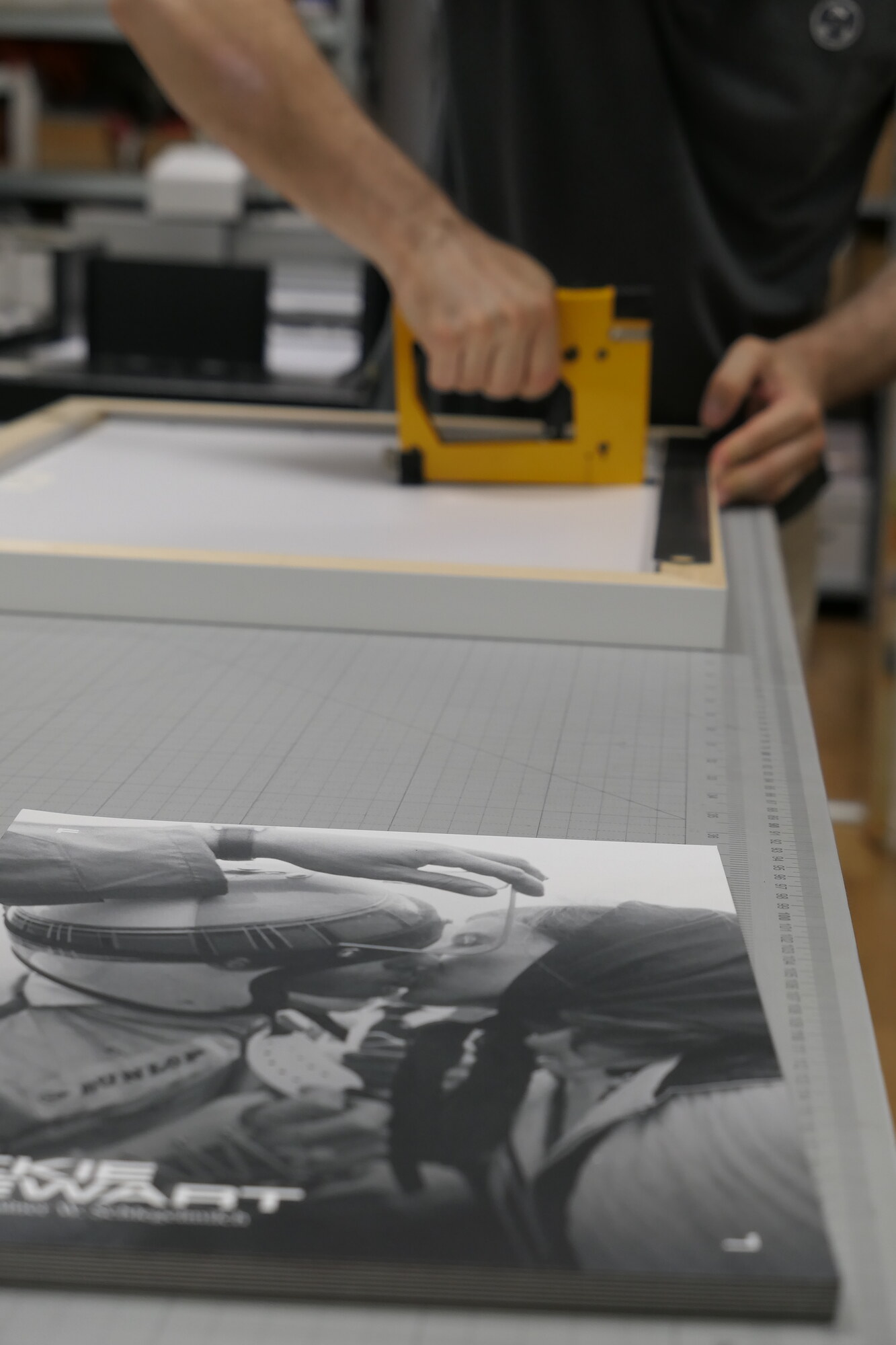 Fixing a frame with a framing tacker. Printed covers are stacked in the foreground.
