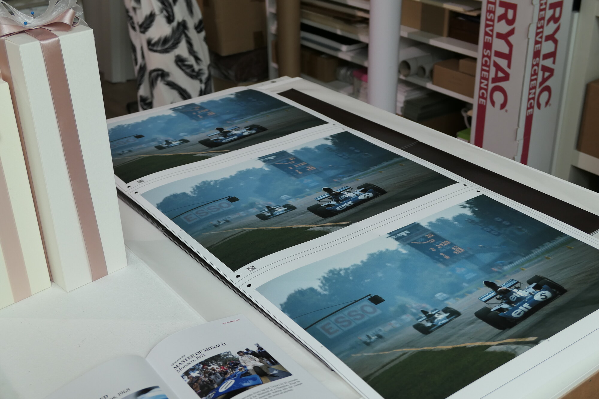 Proofs of one spread laid out for checking, beside ribbon-tied boxes and an open booklet.